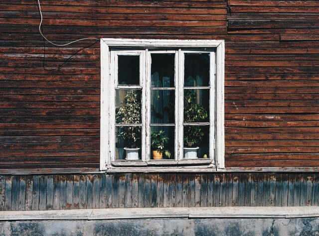 An unkempt wooden window. Paint is peeling and the wooden facade is showing signs of water and UV wear.