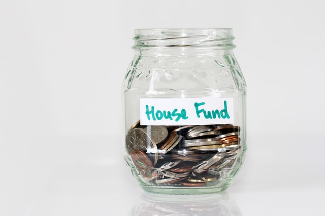 A mason jar lacking a lid is partially filled with coins and bears the label "House Fund" in hand-written lettering. It appears that the coins are Euros, but I am hoping no one looks too closely. If they do, one of the coins reads (for marketing purposes) BC Hydro Rebate.