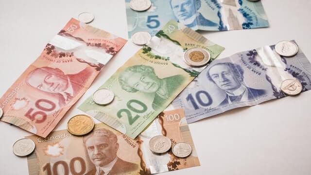 Colourful Canadian Cash and Coins Clutter the cover of a clear background.