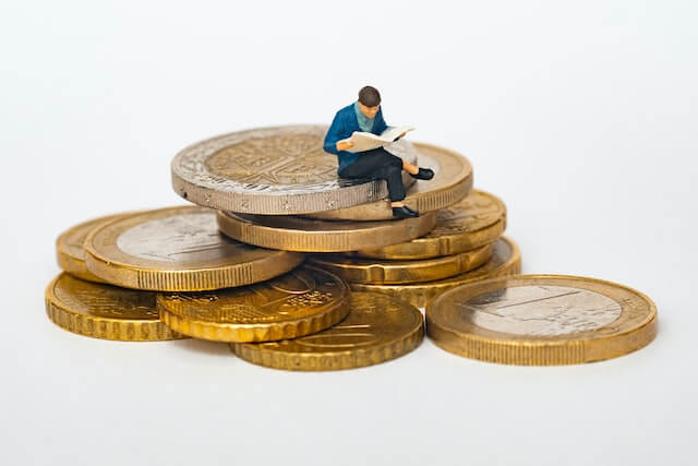A small figure is reading while sitting on a stack of coins.