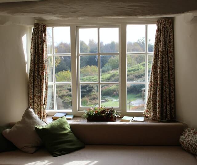 A large wooden window looks out on a picturesque hillside. 