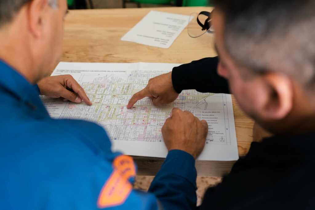 Two people pointing at blueprints on a table. This is supposed to represent a consultation with a contractor.